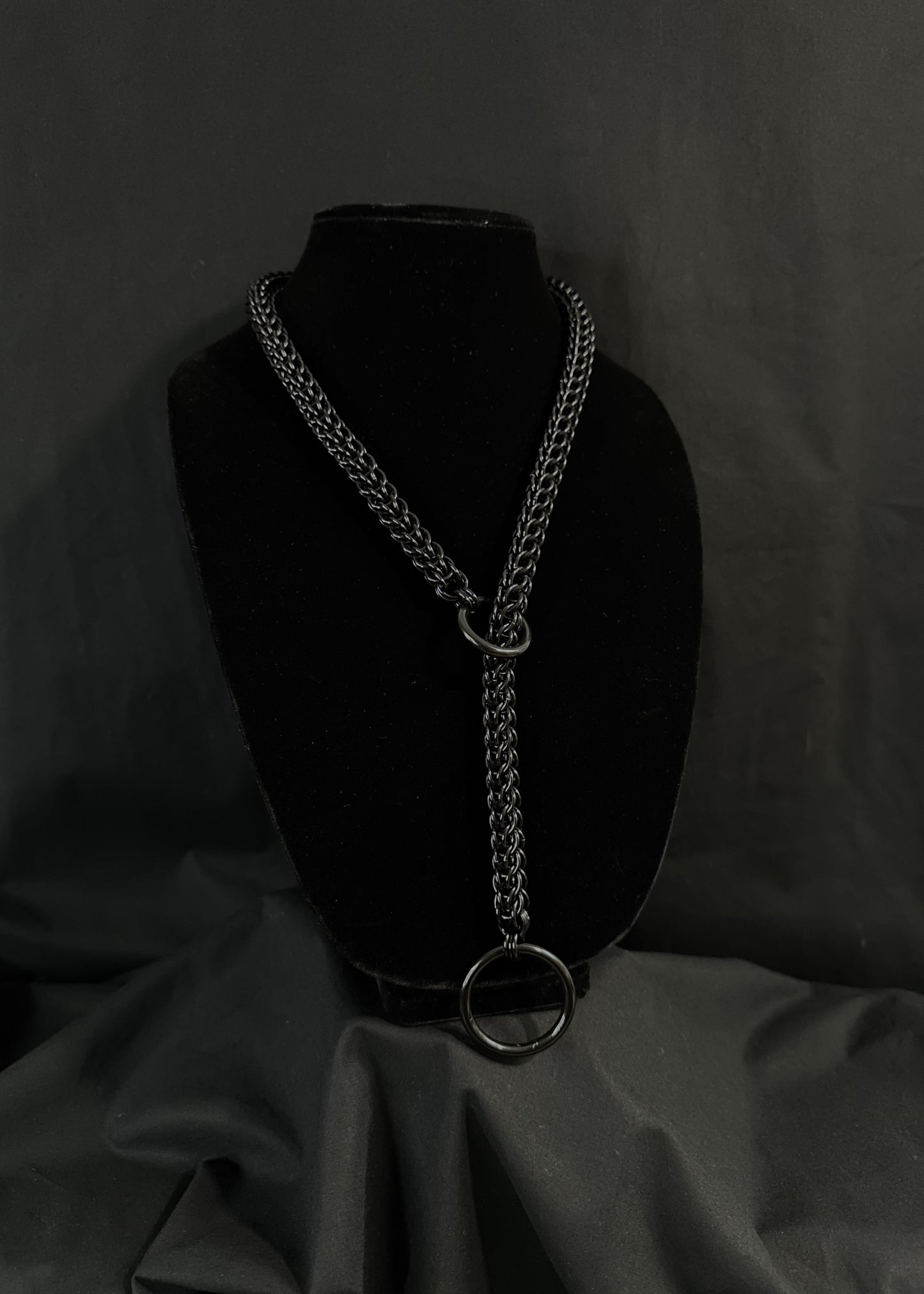 A black choke collar necklace made of anodized aluminum rings displayed on a mannequin.